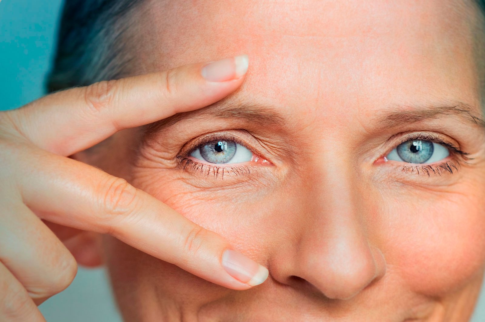Close do rosto de uma mulher madura sorrindo e apontando para os olhos com os dedos em formato de V, celebrando a visão clara e nítida após cirurgia de catarata na Clínica de Olhos da Cidade em Botafogo, RJ