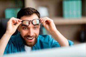 Homem sorrindo e levantando os óculos de grau com expressão de felicidade, ilustrando os benefícios e as dúvidas sobre o pré e pós-operatório da cirurgia refrativa a laser.